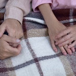 Two pairs of hands on top of a knitted blanket