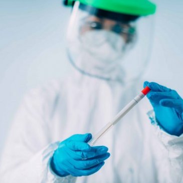 health worker in protective equipment holding a vaccine syringe