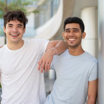 Two young men smiling with one's elbow on the others shoulder
