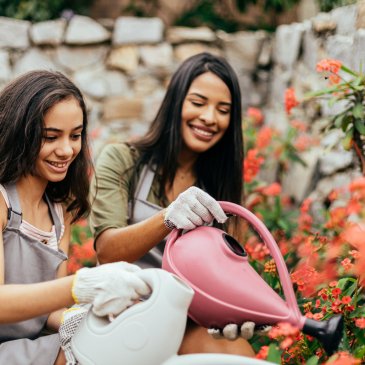 Two women smiling and holding watering cans watering flowers